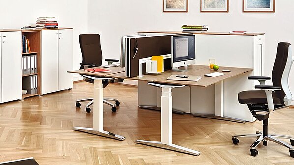 Büroeinrichtung mit höhenverstellbare Schreibtische mit ergonomischen Bürostühlen in hellem Ambiente.