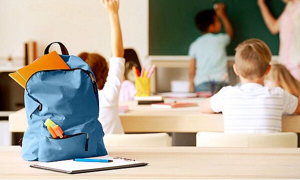 Blauer Rucksack auf einem Tisch, umgeben von Schulmaterial. Ideal für Materialien in der Schule. 