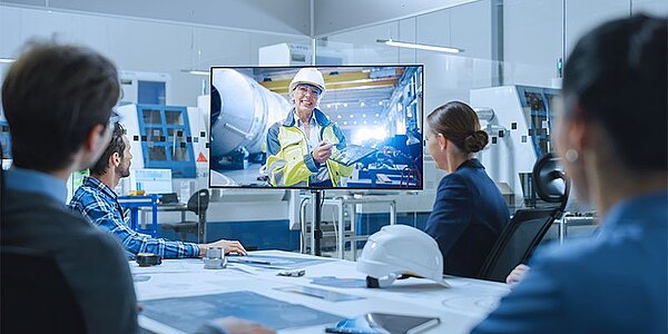 Virtuelles Meeting mit AV-Technik: Ingenieur spricht mit Team über Projekte am Bildschirm.
