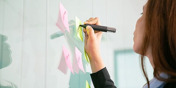Eine Frau verwendet bunte Haftnotizen und Textmarker an Planungswand – Planung für Bürobedarf und Büromaterial.
