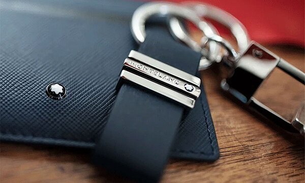 Elegante Lifestyle Accessoires: Schlüsselanhänger aus Leder mit Montblanc-Branding und glänzenden Metallakzenten auf Holzoberfläche.