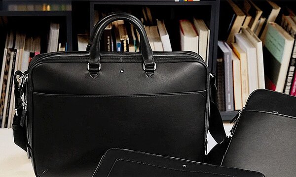 Schwarze Aktentasche neben weiteren Business Accessoires auf einem Tisch für den Büroalltag.